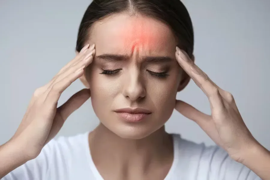 Woman with her eyes closed pressing her fingertips to her temples, forehead highlighted red to show headache pain