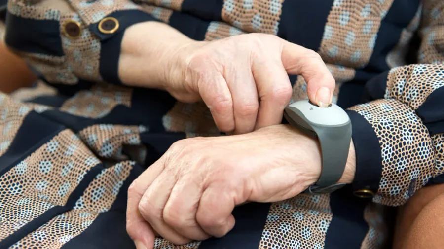 Close-up of an older adult's hands pressing the button on a wrist-worn medical alert device