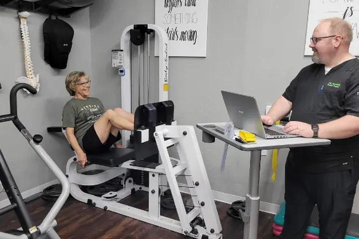 A patient using strength equipment on the treatment floor, supervised by a Dr. Pepper Physical Therapy team member